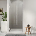 Modern bathroom with a glass shower enclosure, plant, and small table with items.